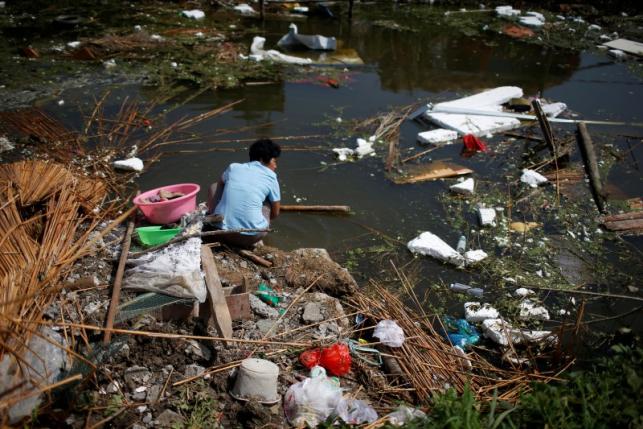 A villager washes shoes in a river covered with debris after a tornado hit Funing on Thursday, in Yancheng, Jiangsu province, June 25, 2016. REUTERS/Aly Song